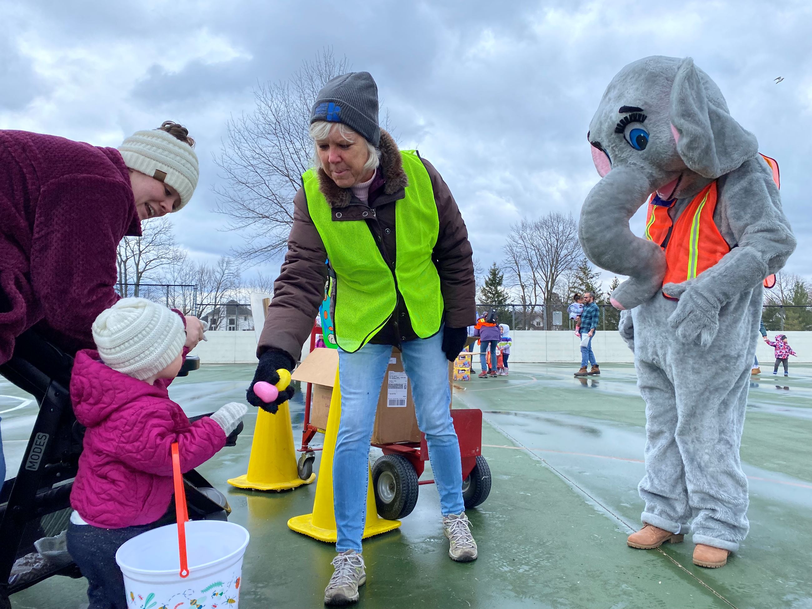 Volunteer handing out an Easter Egg, an elephant stands behind her